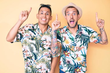 Yazlık şapka ve Hawaii gömleği giyen iki genç eşcinsel adam şaşkın şaşkın ve şaşırmış ve parmaklarıyla işaret ediyor ve kollarını kaldırıyordu.. 