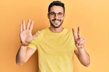 Gündelik kıyafetler giyen ve gözlük takan genç İspanyol adam yedi numaralı parmaklarını gösterip işaret ederken kendine güvenen ve mutlu bir şekilde gülümsüyor.. 