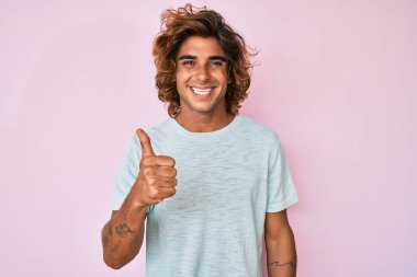 Gündelik kıyafetler giyen genç İspanyol adam elleriyle mutlu bir jest yapıyor. Kameraya bakıp başarıyı gösteren ifade. 