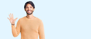 Yakışıklı İspanyol adam gündelik süveter giyer ve beş numarayı göstererek gülümserken kendinden emin ve mutlu.. 