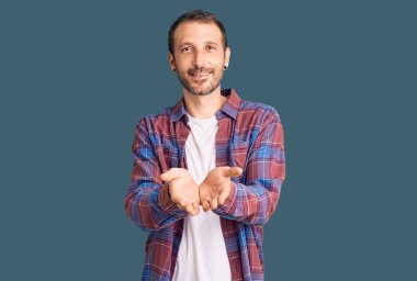 Elleri avuçlarında gülümseyen, sıradan kıyafetler giyen genç yakışıklı adam el hareketi yapıyor ya da yapıyor. Bekleme ve koruma 