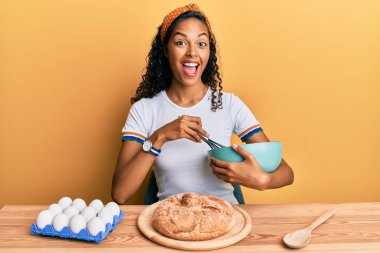 Genç Afrikalı Amerikalı kız masada oturmuş çılgınlığı kutluyor ve şaşırmış bir şekilde gözleri açık heyecanla haykırıyor.. 