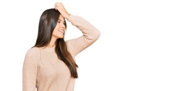 Kış süveteri giyen genç esmer kadın gülümseyerek saçlarına dokunarak el hareketleriyle çekici ve şık bir poz veriyor. 