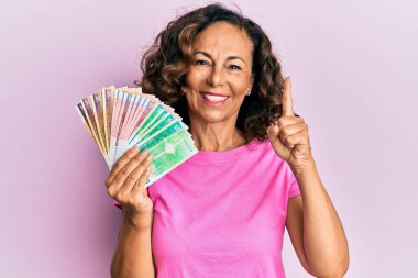 Orta yaşlı İspanyol kadın elinde Norveç kronu banknotları tutarken bir fikir veya soruyla gülümsüyor ve mutlu bir yüzle işaret ediyor. 