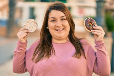 Genç İspanyol artı iri kadın gülümseyerek şehirde pirinç keki ve çörek tutuyor..