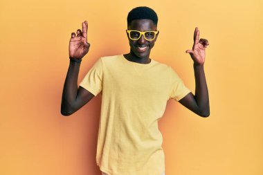 Sıradan kıyafetler ve gözlük takan Afro-Amerikan genç adam umut ve gözler kapalı gülümseyerek el sallıyor. Şans ve batıl inançlar. 