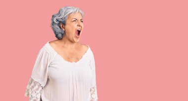Senior woman with gray hair wearing bohemian style angry and mad screaming frustrated and furious, shouting with anger. rage and aggressive concept. 