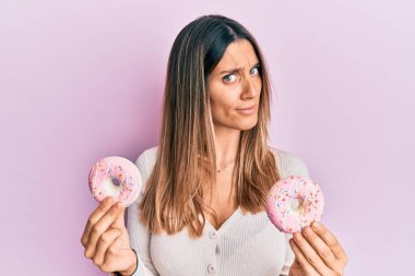 Elinde lezzetli pembe çörekler tutan esmer genç bir kadın. Hiçbir şeyden habersiz ve kafası karışık. şüphe kavramı. 