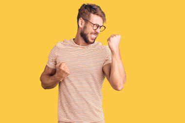 Gündelik giysiler ve gözlük takan genç beyaz adam kolları havada ve gözleri kapalı bir şekilde başarıyı kutluyor ve şaşırıyor. Kazanan konsept. 