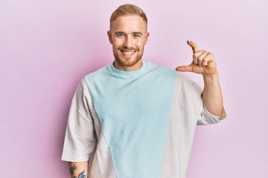 Gündelik kıyafetler giyen, gülümseyen, kendine güvenen, el hareketi yapan, parmaklarıyla işaret yapan ve kameraya bakan genç beyaz bir adam. ölçüm kavramı. 