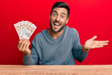 Yakışıklı İspanyol adam Yuan Çin banknotlarını tutuyor başarıyı mutlu bir gülümsemeyle kutluyor ve kazanan el kaldırarak ifade ediyor 