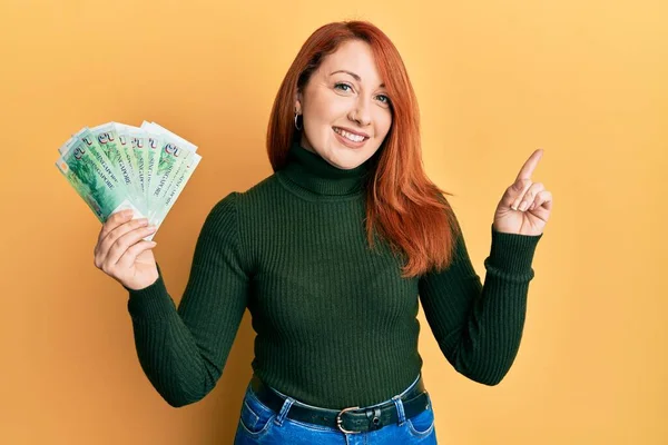 Mulher Ruiva Bonita Segurando Notas Dólares Singapore Sorrindo Feliz Apontando — Fotografia de Stock