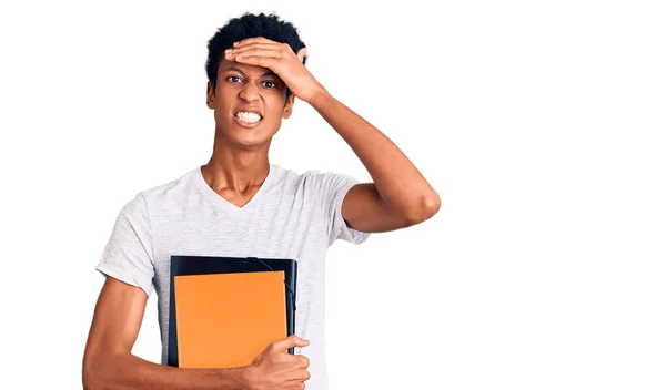 若いアフリカ系アメリカ人の男は本を持っているストレスと頭の上に手で不満 驚きと怒っている顔 — ストック写真