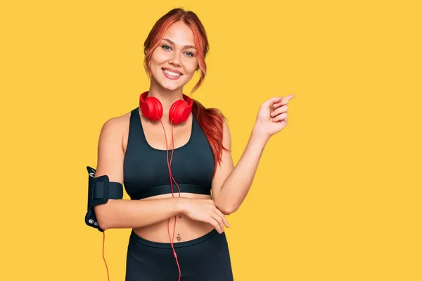 Joven Pelirroja Vistiendo Ropa Gimnasio Usando Auriculares Sonriendo Feliz Señalando —  Fotos de Stock