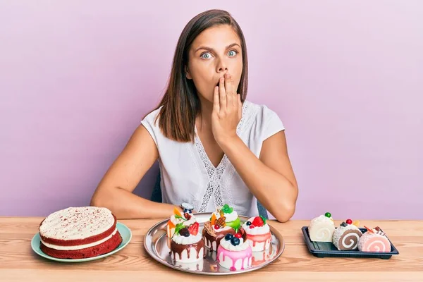 Mulher Caucasiana Jovem Comendo Doces Cobrindo Boca Com Mão Chocado — Fotografia de Stock