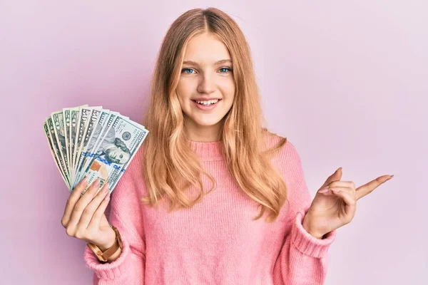 Hermosa Chica Caucásica Joven Sosteniendo Dólares Sonriendo Feliz Señalando Con — Foto de Stock