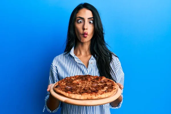 Beautiful Hispanic Woman Holding Tasty Pepperoni Pizza Making Fish Face — 图库照片