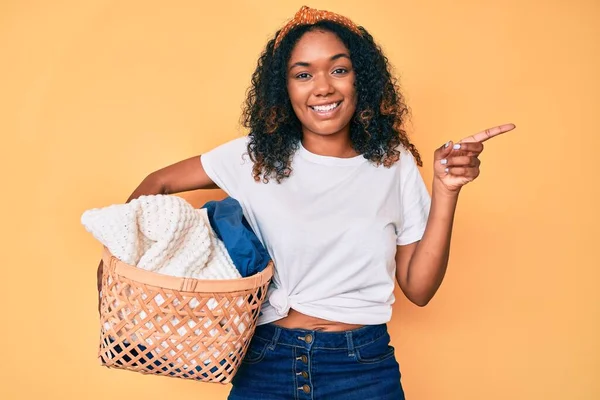 若いアフリカ系アメリカ人の女性を保持洗濯バスケット笑顔幸せなポインティングで手と指で側面 — ストック写真