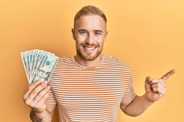 Young Caucasian Man Holding Dollars Smiling Happy Pointing Hand Finger — Stock Photo, Image