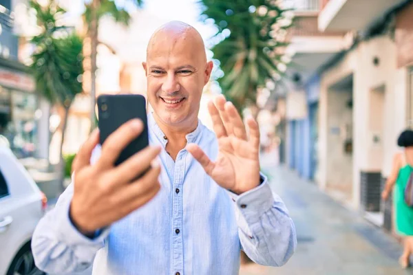 Middle age bald man smiling happy doing video call using smartphone at the city.