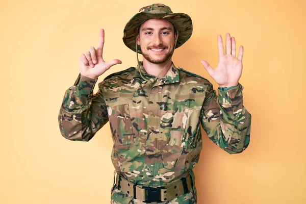 自信と幸せ笑顔ながら カモフラージュ軍の制服を身に着けている若い白人男性は指番号7で見せ 指摘します — ストック写真