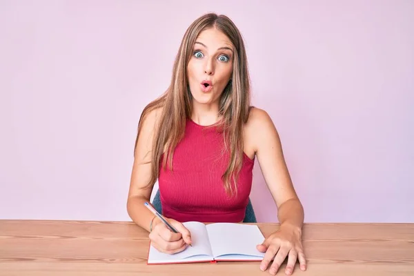 Young Caucasian Girl Writing Notebook Sitting Table Scared Amazed Open — Foto de Stock