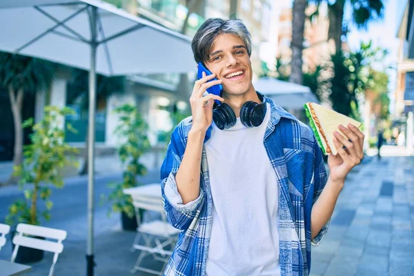 Jonge Spaanse Man Lacht Gelukkig Praten Smartphone Het Eten Van — Stockfoto