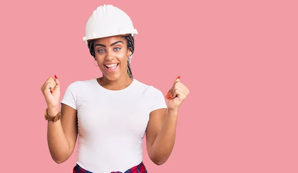 身穿硬礼帽 穿着建筑工人服装的年轻非洲裔美国女人自豪地尖叫着 高举双臂庆祝胜利和成功 — 图库照片
