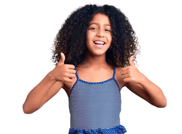 手で積極的なジェスチャーを行う水着の成功サインを着て巻き毛を持つアフリカ系アメリカ人の子供 親指を笑顔と幸せ 陽気な表情と勝者のジェスチャー — ストック写真