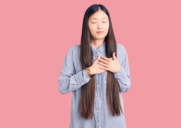 若い美しい中国の女性は 閉じた目と顔に感謝のジェスチャーで胸に手で笑みを浮かべてカジュアルなシャツを着て 健康の概念 — ストック写真