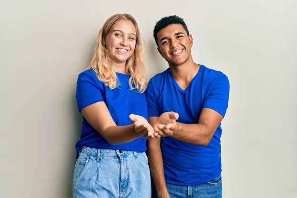 Young interracial couple wearing casual clothes smiling with hands palms together receiving or giving gesture. hold and protection