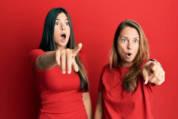 西班牙裔家庭的母亲和女儿穿着便服 穿着红色背景的衣服 手指指向前方 满口惊讶的表情 前面有什么东西 — 图库照片