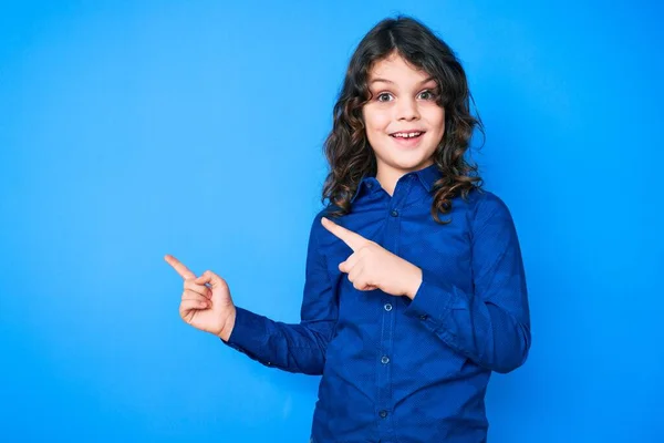 カジュアルな服を着て長い髪をしたかわいいヒスパニック系の子供は笑顔とカメラを見て2本の手と指で側面を指して — ストック写真