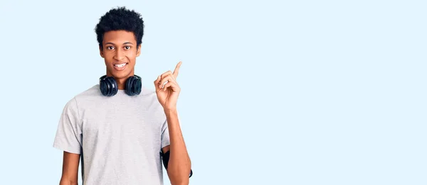 若いアフリカ系アメリカ人の男性は ジムの服を着て 成功したアイデアで指を指してヘッドフォンを使用します 興奮して幸せよ 第1位 — ストック写真