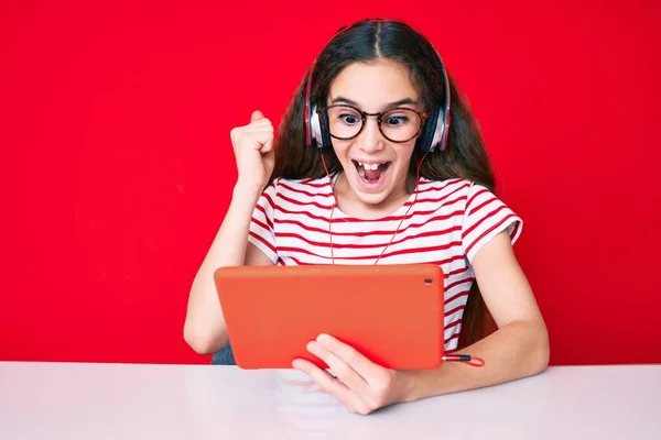 Cute Hispanic Child Girl Using Touchpad Headphones Sitting Table Screaming — Stok fotoğraf