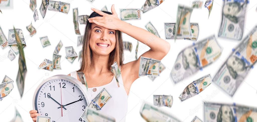 Young beautiful girl holding big clock stressed and frustrated with hand on head, surprised and angry face