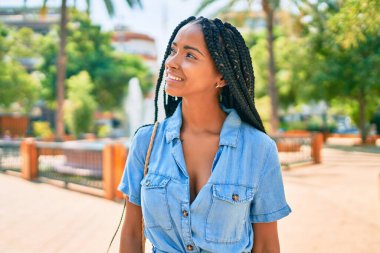 Genç Afrikalı Amerikalı kadın gülümseyerek parkta mutlu bir şekilde yürüyor..