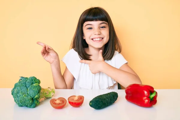 若いです女の子ともに座っているテーブルの上に野菜笑顔とカメラを見てポインティングで二つの手と指へ側 — ストック写真