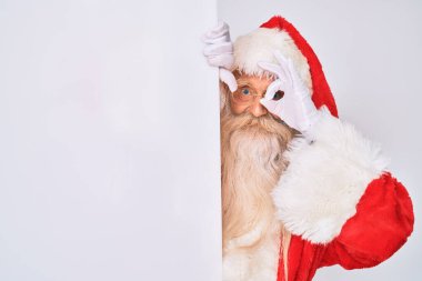 Gri saçlı, uzun sakallı, Noel Baba kostümü giyen, elinde bayrak tutan mutlu mesut gülümseyen, el pençe divan duran yaşlı bir adam. 