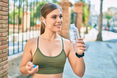 Genç sarışın sporcu şehirde bir şişe su içerek egzersiz yapıyor..