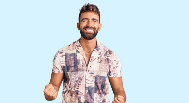 İspanyol asıllı genç adam, yaz kıyafetleri içinde çok mutlu ve heyecanlı bir şekilde kollarını kaldırıp, gülümseyip, başarı çığlıkları atarak zafer jesti yapıyor. kutlama konsepti. 