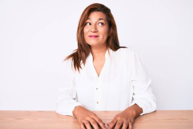 Orta yaşlı esmer, İspanyol iş kadını, sıradan beyaz gömlekli, masaya oturmuş gülümseyen ve gözlerini kaçıran.. 