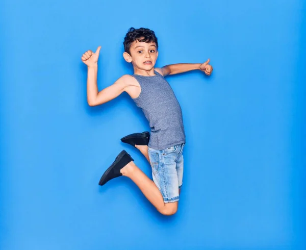 愛らしい子供はカジュアルな服を着ています 青の背景の上に親指でOkサインをジャンプ — ストック写真