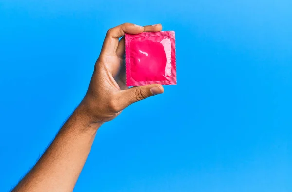 Ung Latinamerikansk Hand Håller Kondom Över Isolerad Blå Bakgrund — Stockfoto