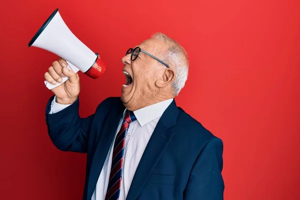 Senior grey-haired businessman screaming using megaphone over isolated red background.