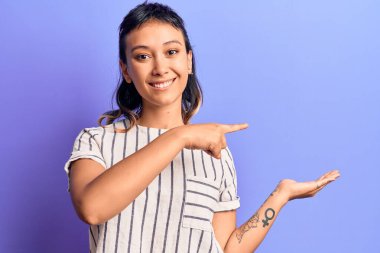 Gündelik giysiler giyen genç bir kadın kameraya hayret eder ve gülümserken elini ve parmağını gösterir.. 