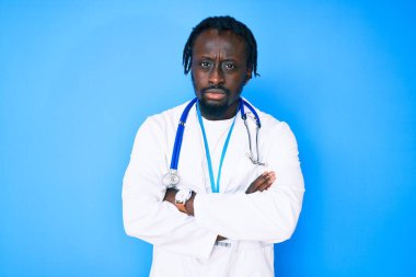 Saç örgülü, doktor steteskobu takan ve kimlik kartı takan, kuşkucu ve gergin, yüzünde çapraz kollu tasvip etmeyen genç Afro-Amerikan bir adam. negatif kişi. 
