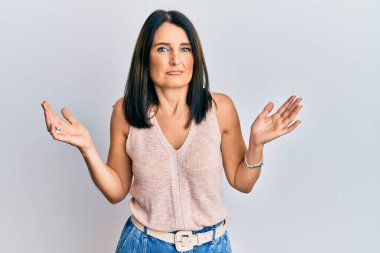 Orta yaşlı esmer kadın gündelik kıyafetler giyiyor ve kolları açık ve kafası karışık, hiçbir fikri yok ve şüpheli bir yüzü var.. 