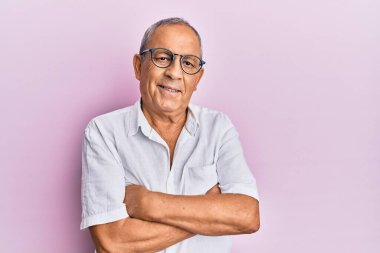 Yakışıklı, olgun, rahat gömlekli ve gözlüklü mutlu yüzlü, kollarını kavuşturup kameraya bakan bir adam. pozitif kişi. 