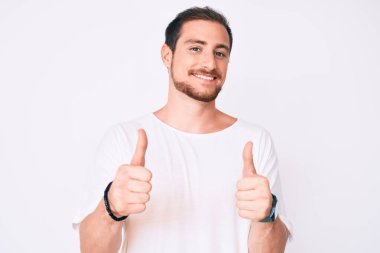 Gündelik beyaz tişört giyen genç, yakışıklı bir adam elinde olumlu bir jest yapıyor, gülümsüyor ve mutlu. Neşeli ifade ve kazanan jest. 